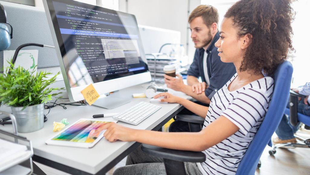 Developing accessible websites requires thoughtful planning. Woman at computer while colleague looks on.
